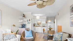 A modern kitchen with white cabinets, a dining area with wicker furniture, and a ceiling fan.