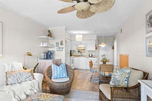 Une cuisine moderne avec des meubles blancs, un coin repas doté de meubles en osier et un ventilateur de plafond.