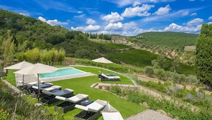 A pool area with lounge chairs and umbrellas, surrounded by lush greenery and vineyards.