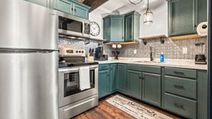Una cocina con armarios azul turquesa, electrodomésticos de acero inoxidable, techo de madera y un felpudo con texto.