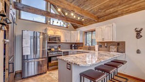 A modern kitchen with stainless steel appliances, a large island with bar stools, wooden ceiling beams, and a brick backsplash. - Mountain Cabin w/VIEWS in Brian Head, Utah! Fun to be had Winter, Summer & Fall! (Brian Head)