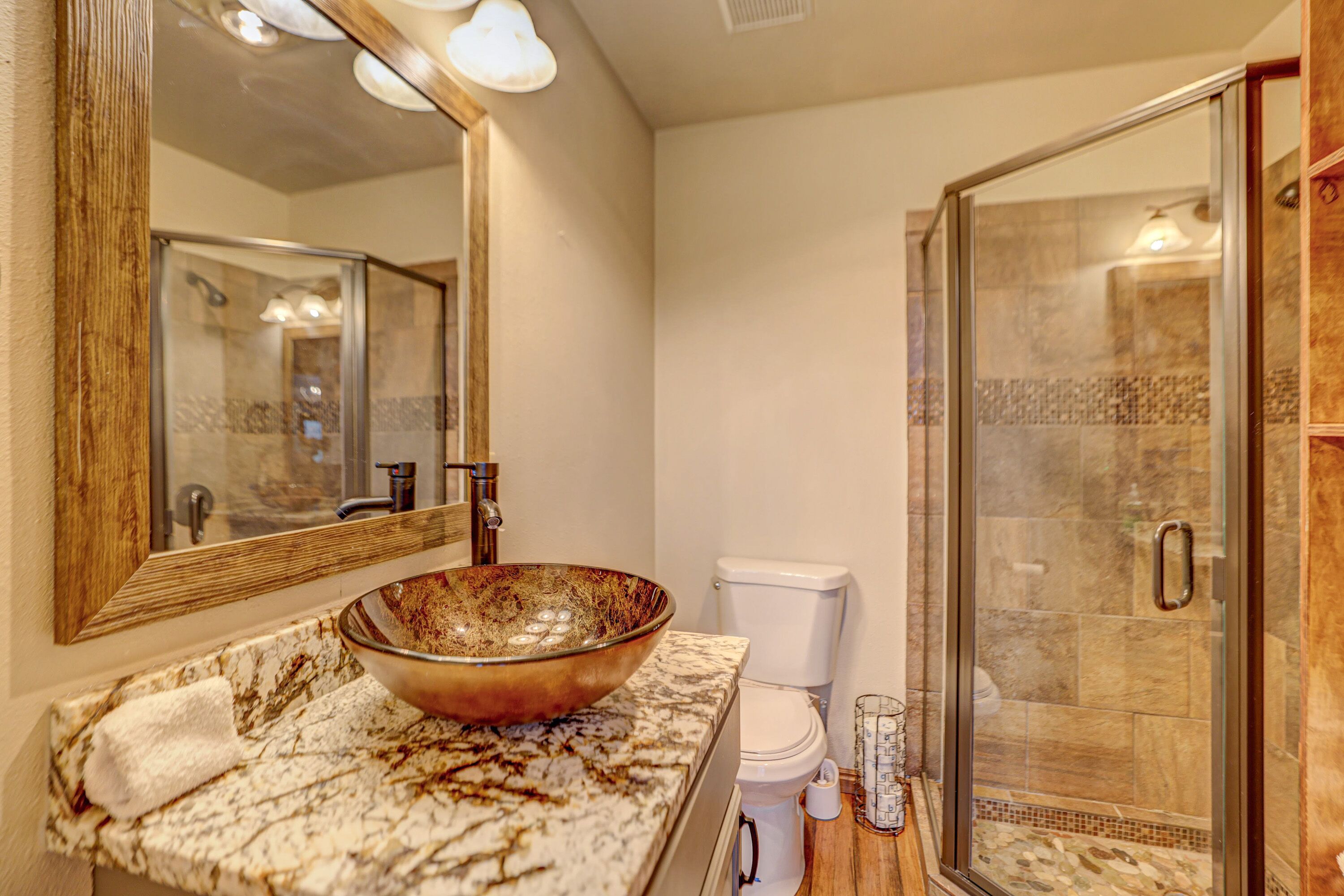 A bathroom with a marble countertop, a large mirror, a glass shower enclosure, and a toilet.
