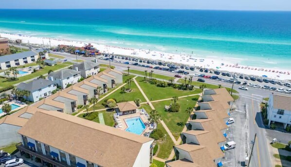 A coastal hotel with a swimming pool, a beach view, and a parking lot.
