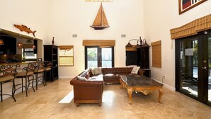 Un salon spacieux avec un canapé en cuir marron, une table basse en bois et un coin repas comprenant un bar et des chaises.