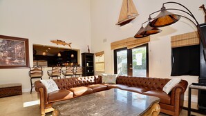 Un vaste salon comprenant un grand canapé d’angle en cuir, une table basse en marbre et un coin repas avec une table et des chaises en bois.