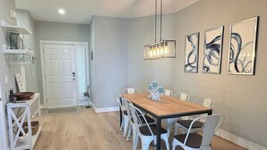 A dining area with a wooden table and white chairs, a hanging light fixture, and abstract art on the wall. - *New*Oceanview, Golf, Pool, Tennis, Beach Access (Corolla)