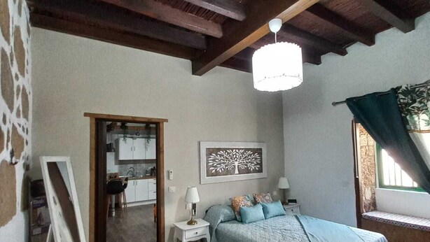 Une chambre à coucher comprenant un lit, une table de chevet, une lampe, un tableau encadré et une fenêtre donnant sur un paysage.