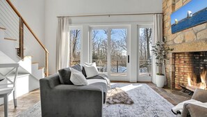 Amplia sala de estar con un sofá gris, chimenea y un ventanal con vistas a un área exterior pintoresca.