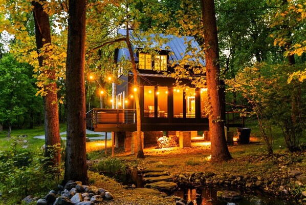 Une cabane dotée d’une terrasse, entourée d’arbres et bordée d’un petit ruisseau.