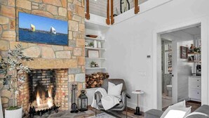 Un salón acogedor con chimenea de piedra, un espacio de descanso cómodo y vistas al mar a través de una ventana.