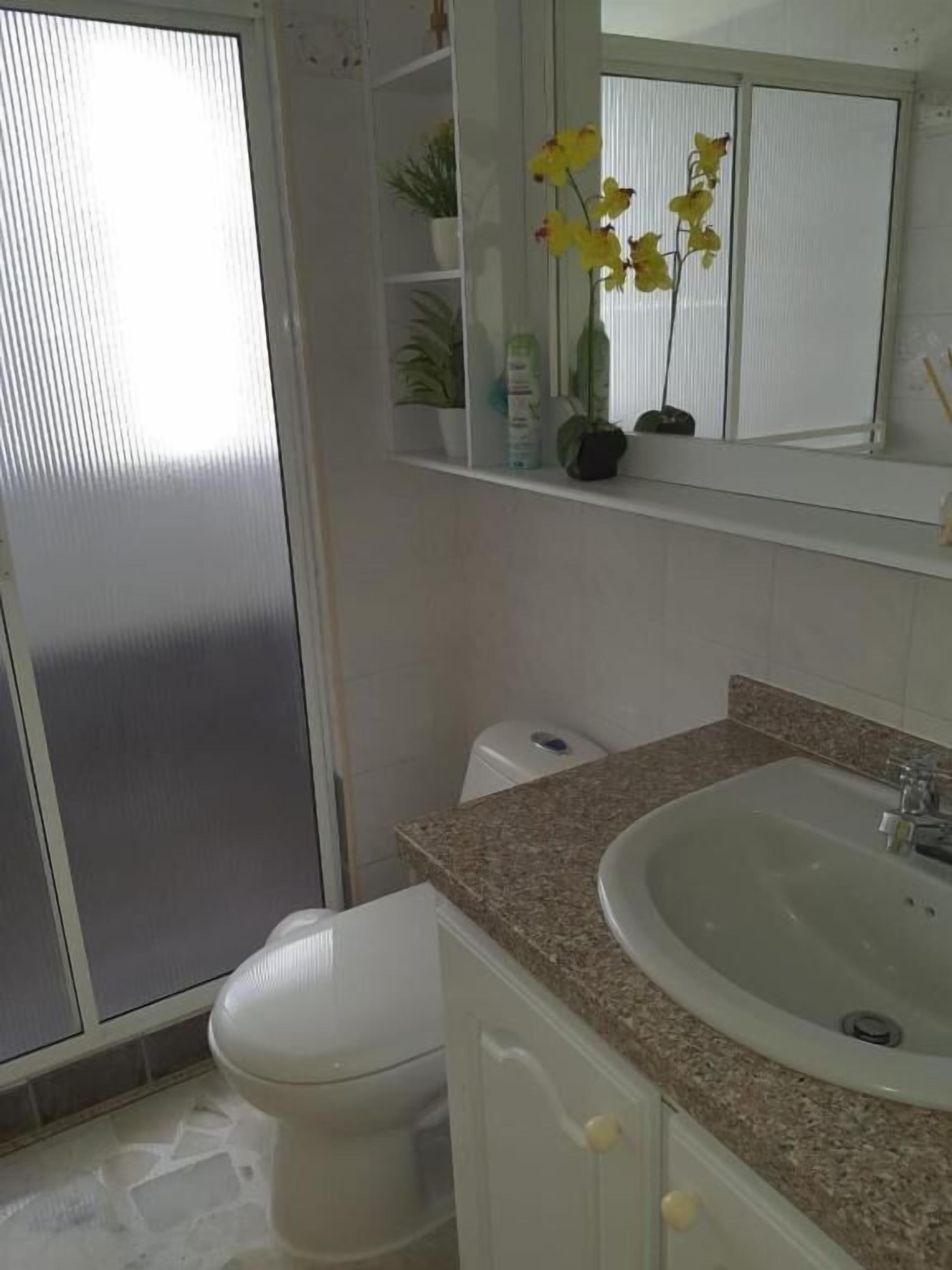 Une salle de bain avec des toilettes blanches, un lavabo doté d’un plan de travail en granit et un miroir au-dessus du lavabo.