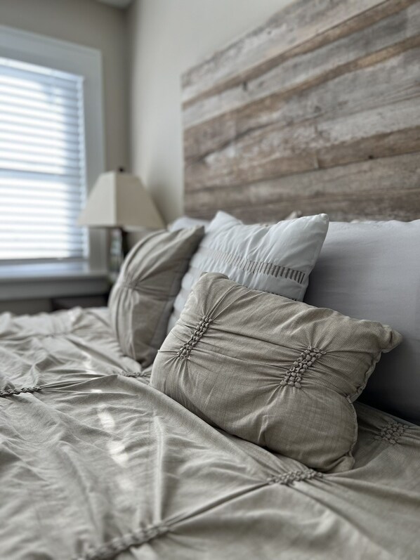 A neatly made bed with a wooden headboard, a lamp on a bedside table, and a window with blinds.