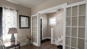 Ein Wohnzimmer mit Holzboden, einer Couch, einem Tisch mit Lampe, einem Fenster mit Vorh ängen und einer Treppe zu einem anderen Raum.