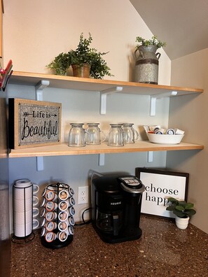 A kitchen counter with a coffee maker, a mug rack, and a sign that says "Life is Beautiful".