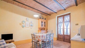 A cozy dining area with a table set for four, surrounded by chairs. A wooden cabinet with glass doors is against the wall, and a television is on a stand to the left.
