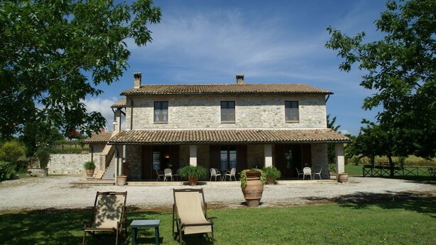 A two-story stone building with a tiled roof, a covered patio with outdoor seating, and a gravel driveway.