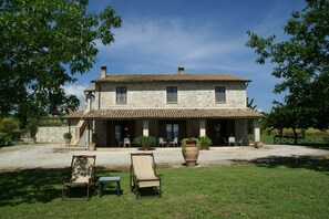 Un bâtiment en pierre de deux étages, doté d’un toit en tuiles, d’un patio couvert avec des sièges extérieurs et d’une allée en gravier.