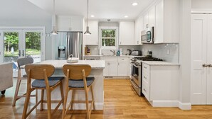 A modern kitchen with white cabinetry, a central island with bar stools, stainless steel appliances, and pendant lighting.
