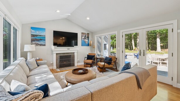 A spacious living room with a large sofa, a fireplace, a television, and a view of the outdoors.