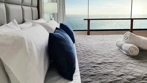 A hotel room with a large bed, a view of the sea, and a balcony with a railing.