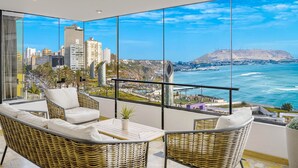 A balcony with wicker furniture, a potted plant, and a view of the city and ocean.