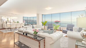 A spacious living area with a large window overlooking a scenic view, furnished with white sofas and a coffee table.