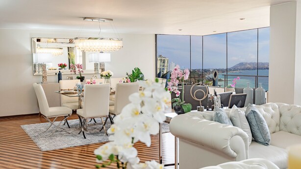 A modern living room with a dining area, large windows with a city and water view, and a cozy seating area.