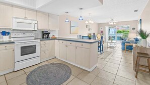 A modern kitchen with white cabinets, a built-in microwave, and a large island with blue pendant lights. - Beach Condo |  Pool | 2 Bedrooms | Monthly Rental (Cape Canaveral)
