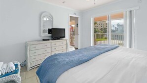 A bedroom with a bed, a dresser, a television, and a balcony with a view. - Beach Condo |  Pool | 2 Bedrooms | Monthly Rental (Cape Canaveral)