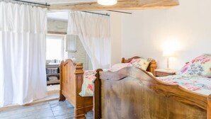 A wooden bed with a floral bedspread in a room with white curtains and a wooden ceiling.