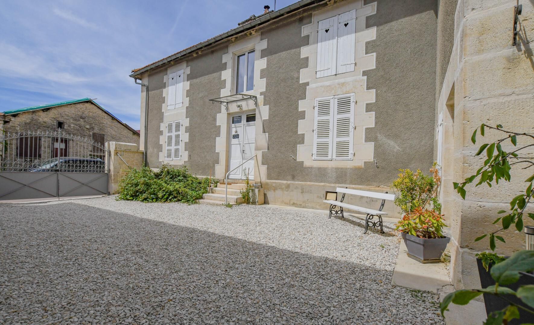 Un bâtiment avec une allée gravillonnée, un banc et un pot de fleurs.