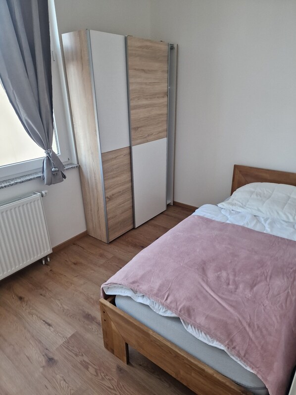 A bedroom with a bed, a wardrobe, a radiator, and a window with curtains.