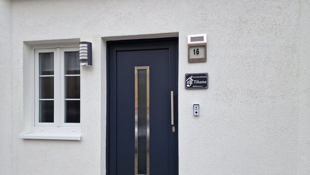 A dark blue door with a vertical handle, a window with multiple panes, and a wall-mounted number plate indicating the address as 16. - Im Stadtzentrum, in der Nähe von Musikschulen (Trossingen)