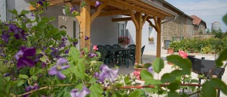 Enjoy outdoor dining or relaxation in this serene patio area with a table and chairs, surrounded by lush plants and flowers.