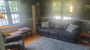 A living room with a sofa, a bench, a rug, a bookshelf, and a window with blinds. - 3 bedroom/2 bath home; close to EAA. Large kitchen and outside deck area  (Oshkosh)