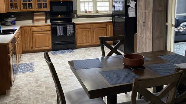 A modern kitchen with wooden cabinets, a black refrigerator, and a dining area with a table and chairs. - 3 bedroom/2 bath home; close to EAA. Large kitchen and outside deck area  (Oshkosh)