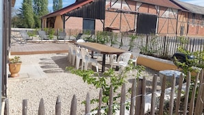 Un espace patio avec une table et des chaises en bois, entouré d’un chemin de gravier et d’une clôture en bois.