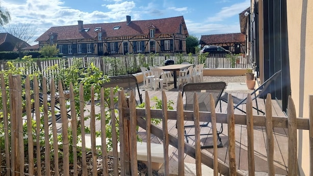 Une cour agrémentée d’une clôture en bois, d’un espace pour s’asseoir en plein air et offrant une vue sur les maisons traditionnelles à colombages qui se dressent à l’arrière-plan.