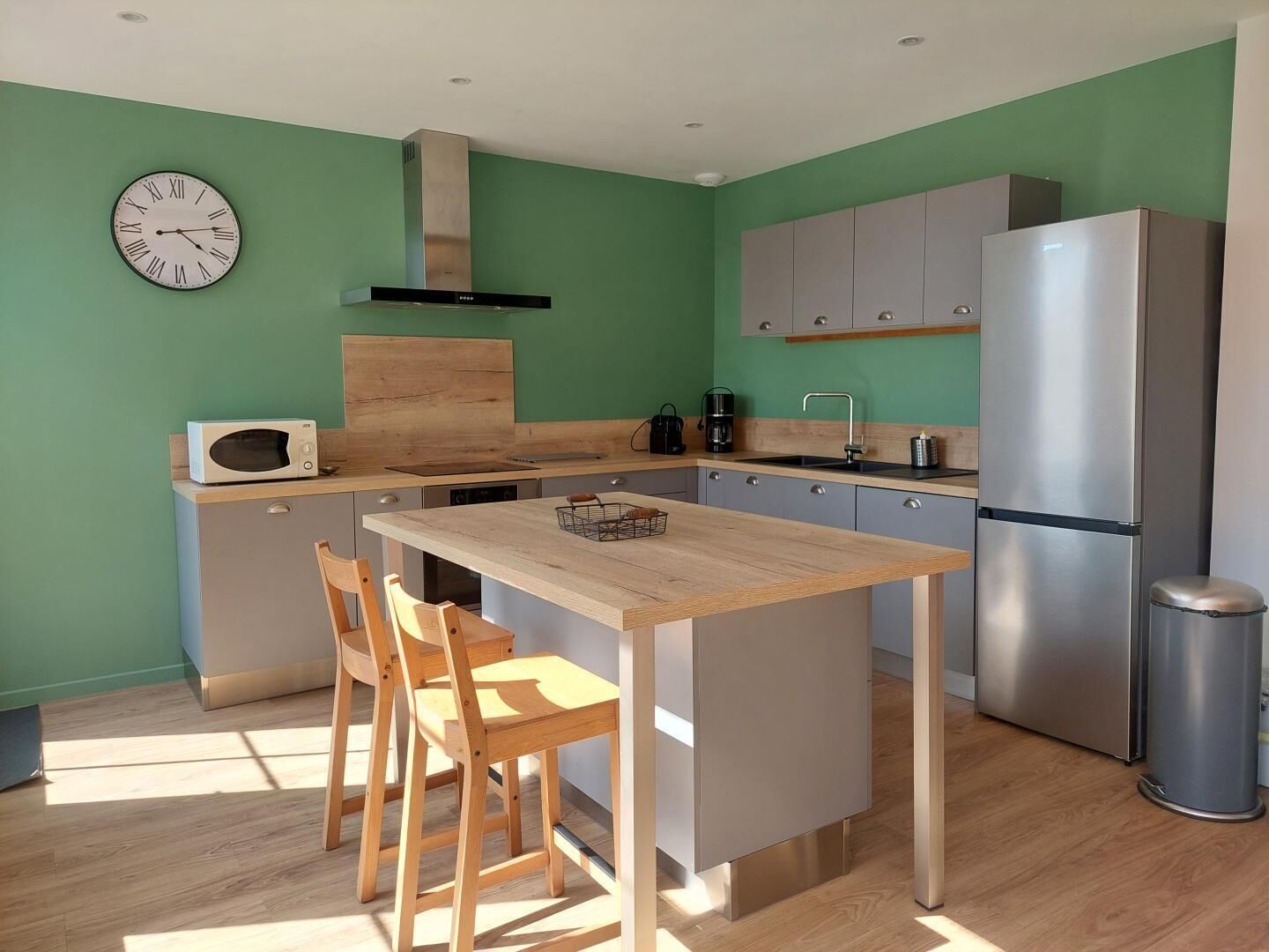 A modern kitchen with a wooden island, two chairs, a microwave, a coffee maker, and a stainless steel refrigerator.