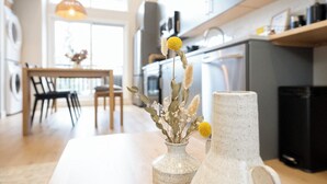 Eine moderne Küche mit einem Holztisch, zwei Keramiktöpfen mit getrockneten Blumen und einer hängenden Pendelleuchte.