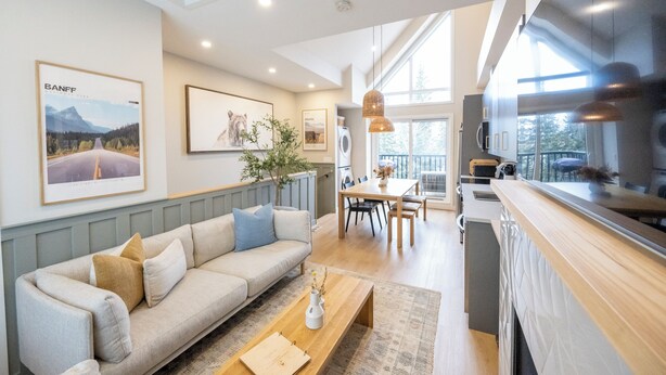 Ein modernes Wohnzimmer mit Sofa, Couchtisch und Essbereich. An den Wänden hängen Bilderrahmen, und ein großes Fenster sorgt für natürliches Licht.