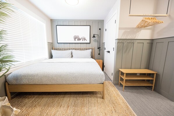 Un dormitorio con una cama de madera, un pequeño banco de madera, una estantería en la pared y un cuadro enmarcado sobre la cama.