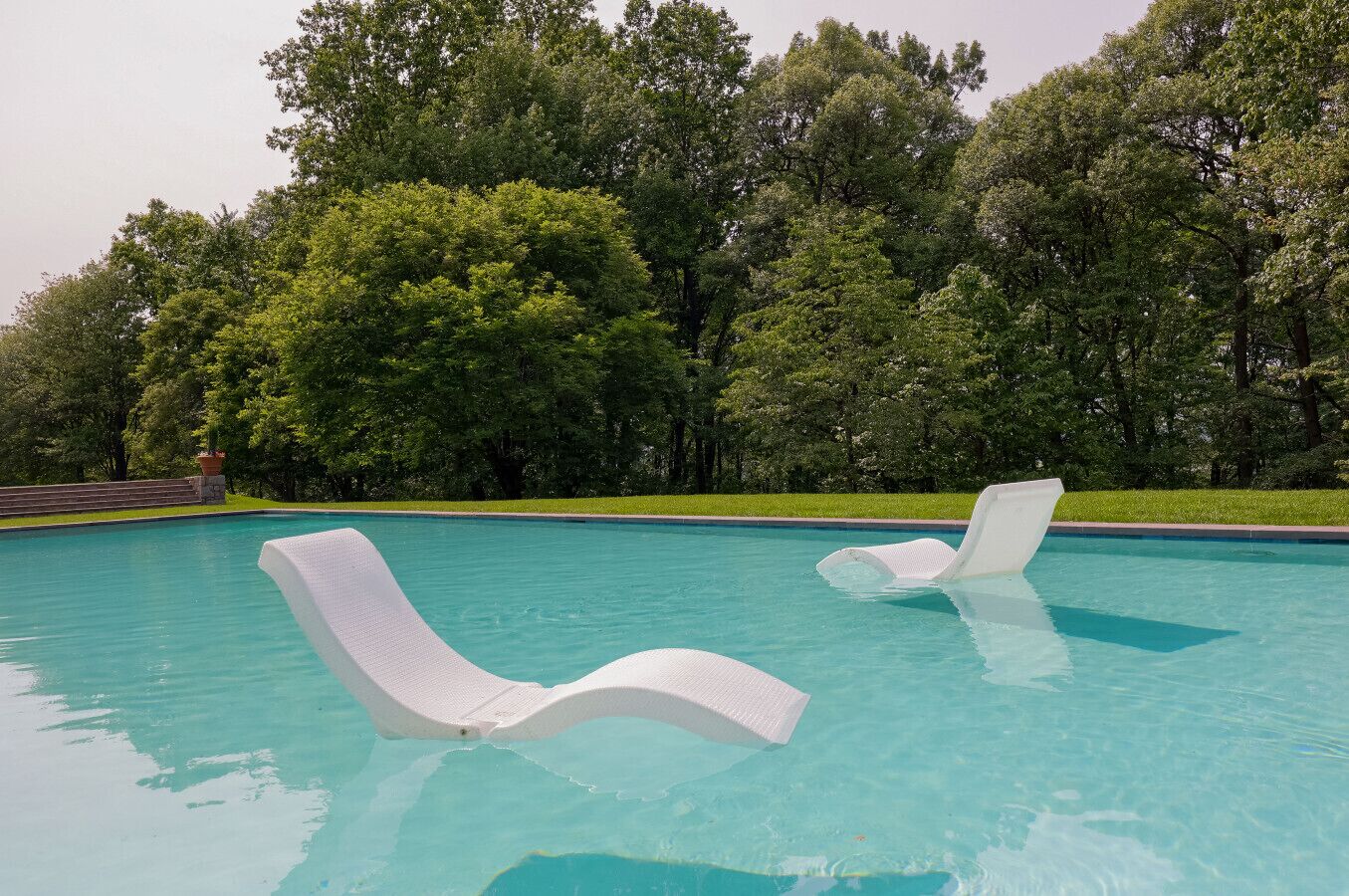 Una piscina con dos sillones blancos.