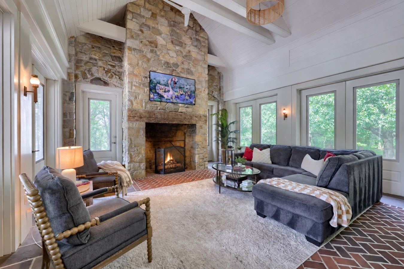 A cozy living room with a stone fireplace, comfortable seating, and large windows.