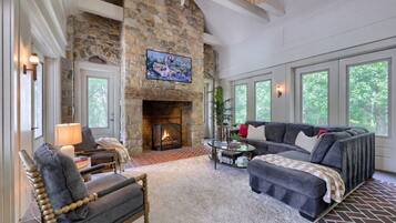 A cozy living room with a stone fireplace, comfortable seating, and large windows.