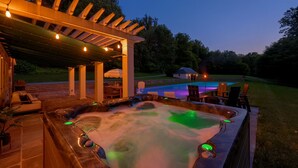 A hot tub area with a pergola overhead, surrounded by outdoor furniture and a pool. - Stone Cottage at Roundtop Estate couples Retreat (Wrightsville)