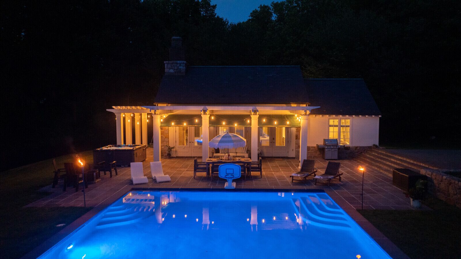 A poolside area with a covered patio, outdoor furniture, and string lights.