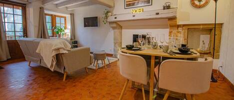 A cozy living room with a sofa, a dining table set for four, and a fireplace.