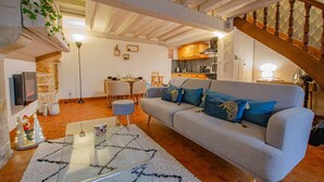 Un saló acollidor amb un sofà gris, una taula de cafè de vidre i una llar de foc. Hi ha una zona de dinar amb una taula i cadires, i una cuina al fons.