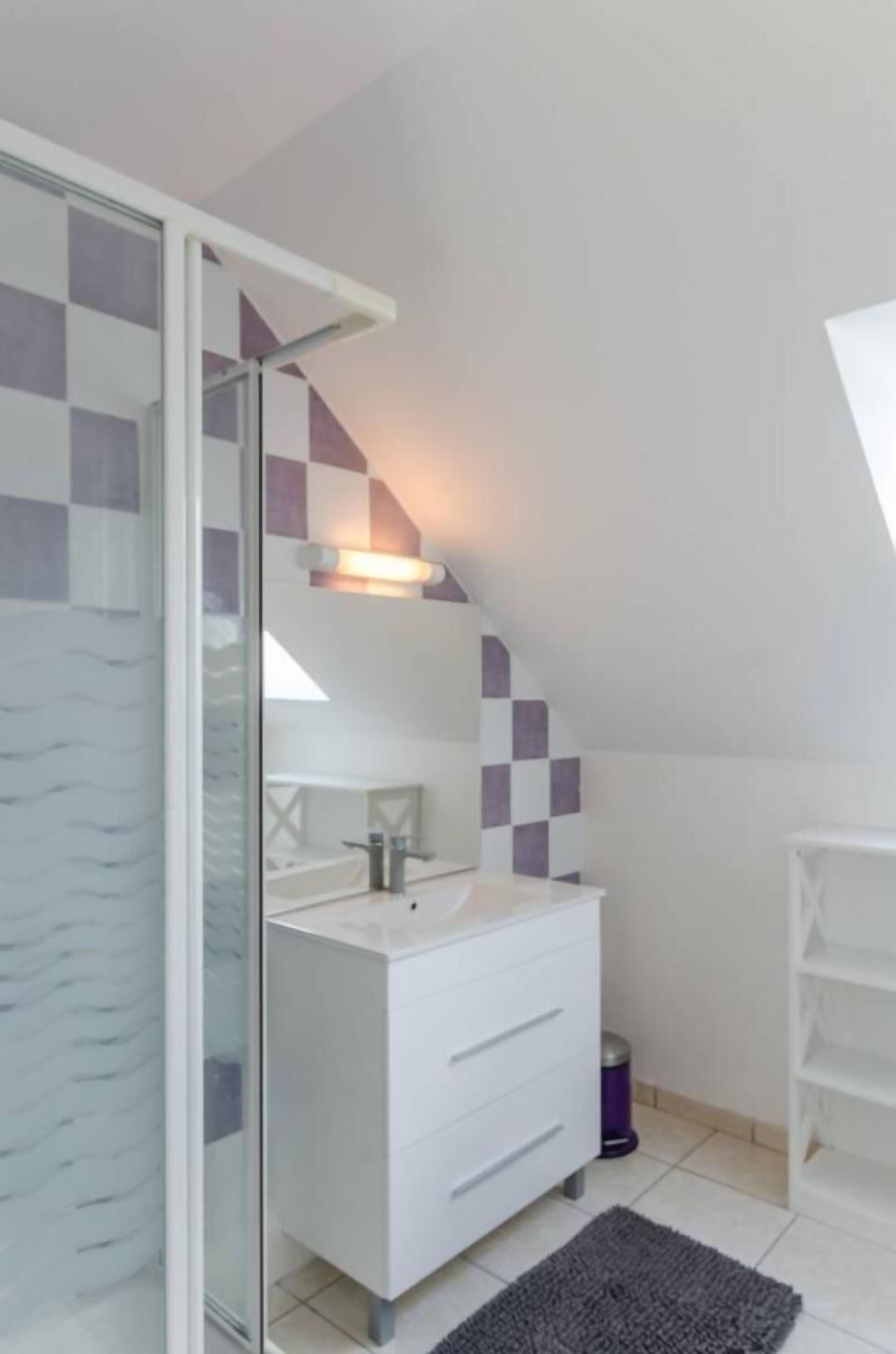 A modern bathroom with a glass shower enclosure, white vanity, and checkered wall tiles.